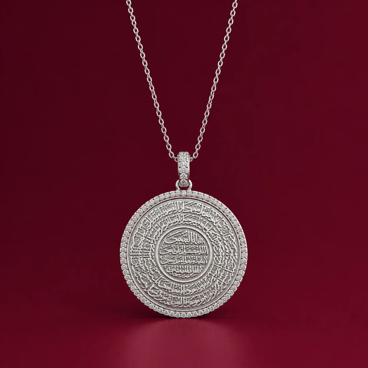 The Ayatul Kursi medallion necklace on a deep burgundy surface.