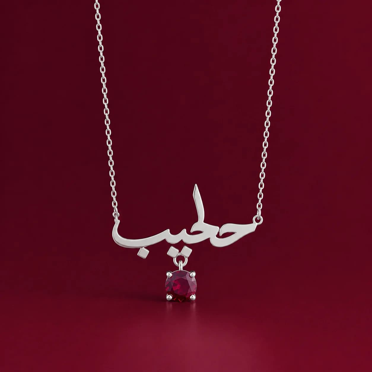 The ruby name necklace on a deep burgundy surface.